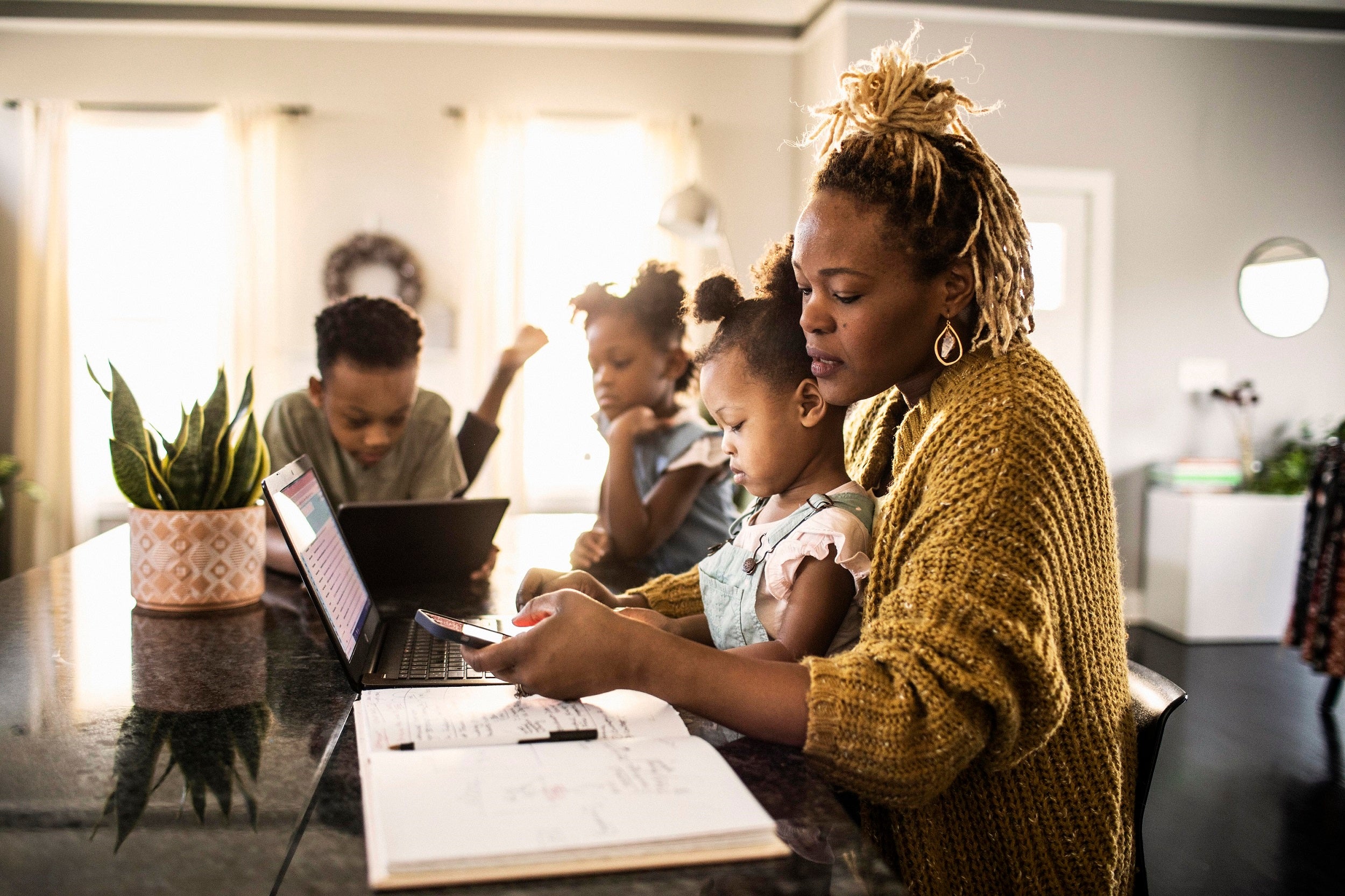 A mother works on her computer at the kitchen counter with her children